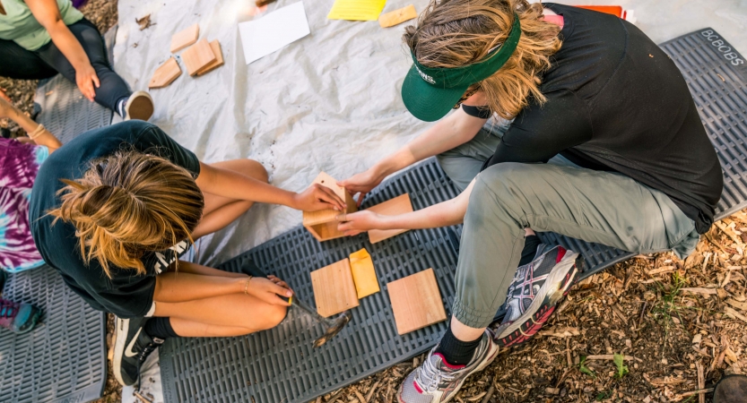 Two people make sandwiches while sitting on pads and a tarp